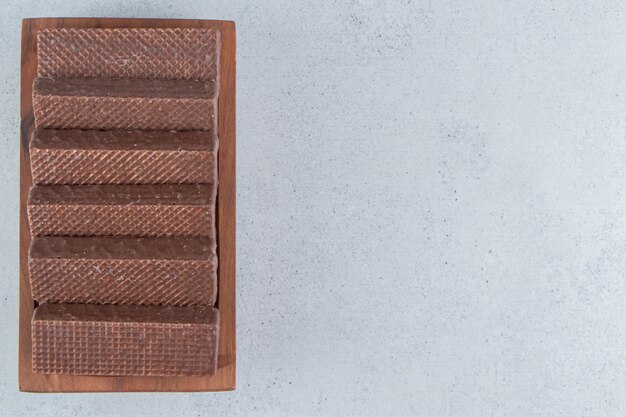 Schokoladenüberzogene Waffeln auf einer hölzernen Platte auf Marmorhintergrund.