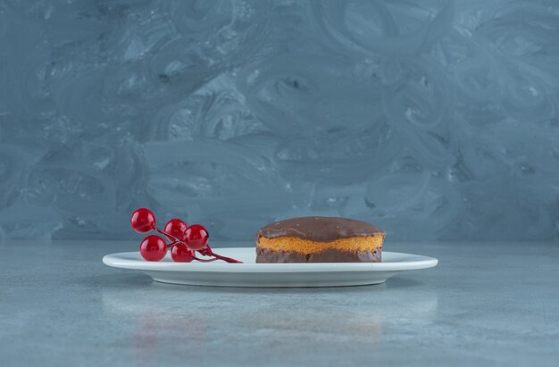 Schokoladenüberzogener Kuchen und eine Gruppe von Weihnachtsbeeren auf einer Platte auf Marmorhintergrund. Hochwertiges Foto