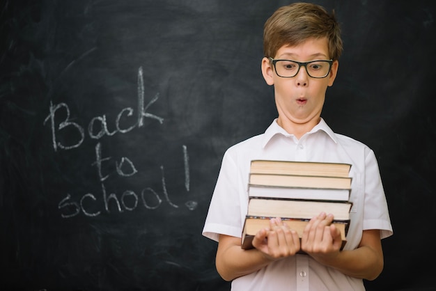 Kostenloses Foto schoolboy hält stapel von büchern stehen