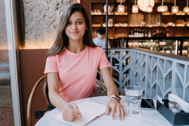 Schreiben einer Molkerei in einer Notiz im Café, Konzept als Erinnerung an das Leben. Frau im Café. Lächelnde Frau, die Notizen Notizblock macht.