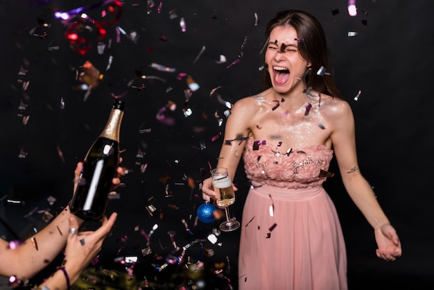 Kostenloses Foto schreiende frau im abendkleid mit glas- und verzierungsball nahe händen mit flasche