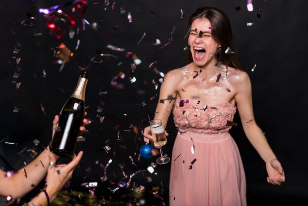 Schreiende Frau im Abendkleid mit Glas- und Verzierungsball nahe Händen mit Flasche