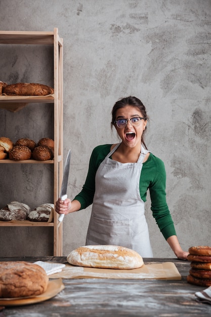 Schreiende junge Bäckerin schnitt das Brot.