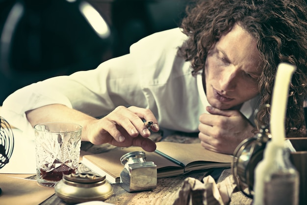 Schriftsteller bei der Arbeit. Hübscher junger Schriftsteller, der am Tisch sitzt und zu Hause etwas in seinen Skizzenblock schreibt