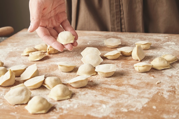 Schritt für Schritt Herstellung von hausgemachten Knödeln, Ravioli oder Pelmeni mit Hackfleischfüllung unter Verwendung von Ravioli-Schimmel oder Ravioli-Hersteller. Bereit zum Kochen von Raviolis auf Holzbrett, Frau Hand hält eine