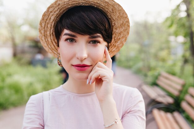 Schüchterne dunkelhaarige Dame mit roten Lippen, die ein silbernes Armband tragen und ihr Gesicht mit dem Finger berühren