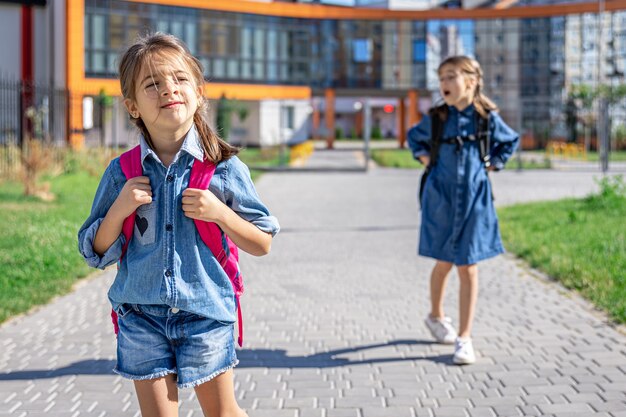 Schüler der Grundschule. Mädchen mit Rucksäcken in der Nähe des Gebäudes im Freien. Beginn des Unterrichts. Erster Herbsttag.