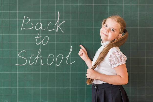 Kostenloses Foto schüler, der zurück auf schuleaufschrift auf tafel zeigt