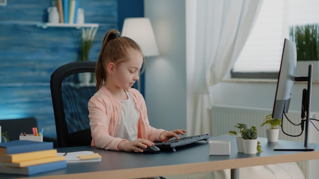 Schüler mit Tastatur und Computer für Online-Unterricht am Schreibtisch. Junges Mädchen, das den Monitor für Schulaufgaben und Hausaufgaben betrachtet. Kleines Kind, das am PC für Fernunterricht und Wissen arbeitet