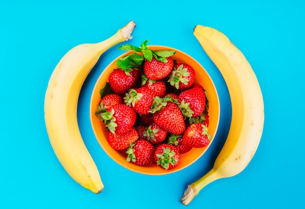 Kostenloses Foto schüssel erdbeeren zwischen den bananen gegen blauen hintergrund