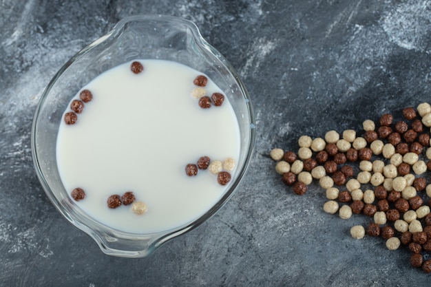 Schüssel frische Milch mit Schokoladenbällchen auf Marmor.