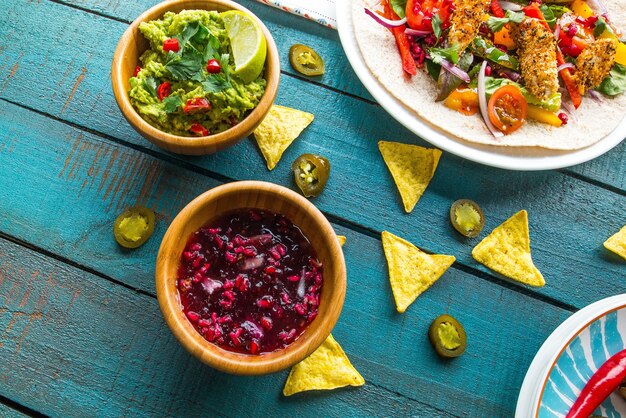 Schüssel Guacamole mit veganem Salat auf einer Pita und Pommes auf einem blauen Holztisch unter den Lichtern