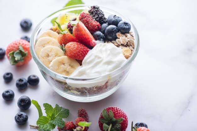 Schüssel Hafergranola mit Joghurt, frischen Blaubeeren, Maulbeeren, Erdbeeren, Kiwi, Banane, Minze und Nussbrett für gesundes Frühstück, Draufsicht, Kopienraum, flache Lage. vegetarisches Lebensmittelkonzept.