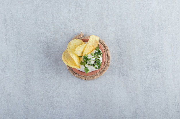 Schüssel Joghurt mit Grüns und Chips auf Stein.