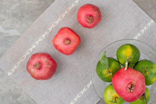 Schüssel Mandarine und Granatapfel auf grauer Tischdecke.
