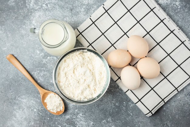 Schüssel Mehl, Eier und Milch auf Marmoroberfläche.