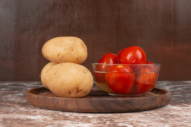 Kostenloses Foto schüssel mit eingelegten tomaten und gekochter kartoffel auf holzteller.