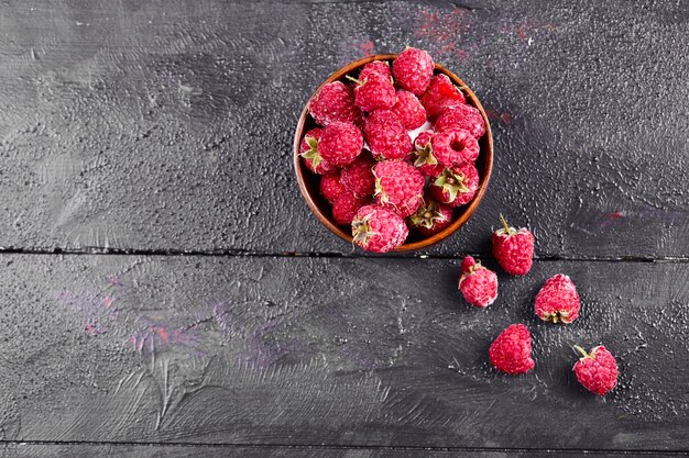 Schüssel mit frischen roten Himbeeren auf dunklem Holztisch.