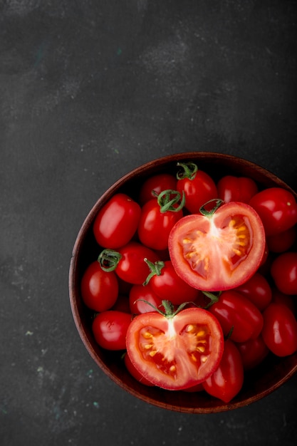 Schüssel mit geschnittenen und ganzen Tomaten auf der rechten Seite auf schwarzer Oberfläche