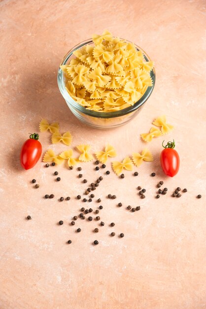 Schüssel mit rohen Nudeln, Pfefferkörnern und frischen Tomaten auf Orange.