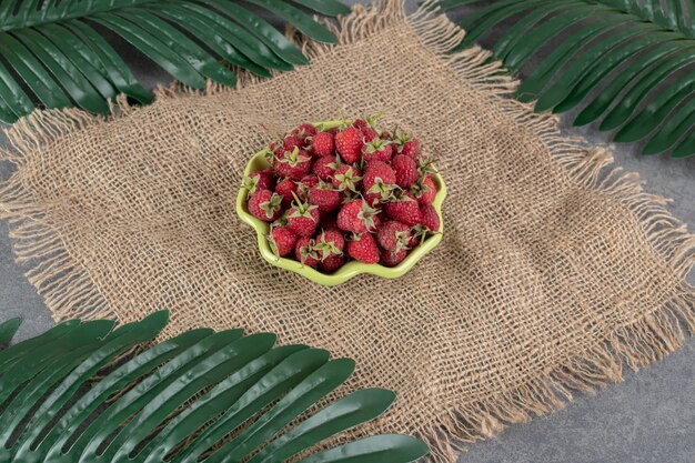 Schüssel mit roten Erdbeeren auf Sackleinen mit Blättern. Foto in hoher Qualität