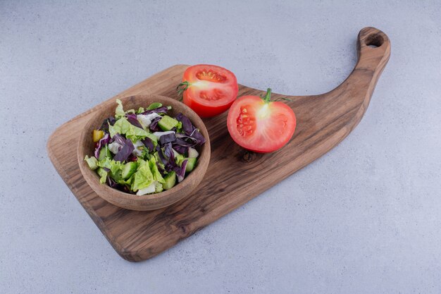 Schüssel mit Salat und in Scheiben geschnittenen Tomaten auf einem Holzbrett auf Marmorhintergrund. Foto in hoher Qualität