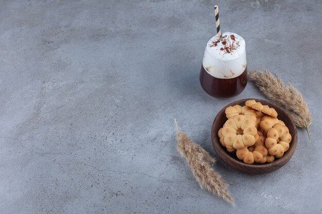 Schüssel mit süßen Keksen mit einem Glas Kaffee auf Marmor.