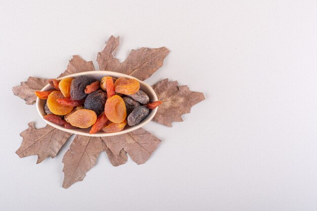 Schüssel mit verschiedenen Bio-Früchten mit trockenem Blatt auf weißem Hintergrund. Foto in hoher Qualität