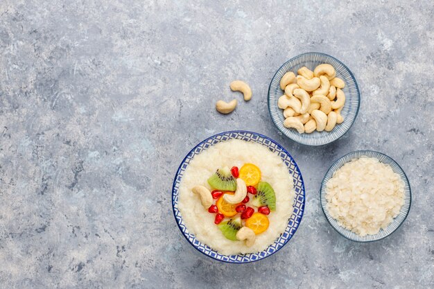 Schüssel Reisflockenbrei mit Kiwischeiben, Granatapfelkernen, Cumquats und Cashewnüssen, Draufsicht