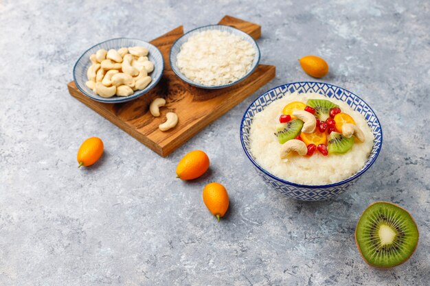 Schüssel Reisflockenbrei mit Kiwischeiben, Granatapfelkernen, Cumquats und Cashewnüssen, Draufsicht