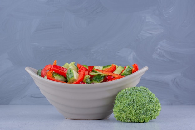 Schüssel salat neben einem stück brokkoli auf marmorhintergrund.