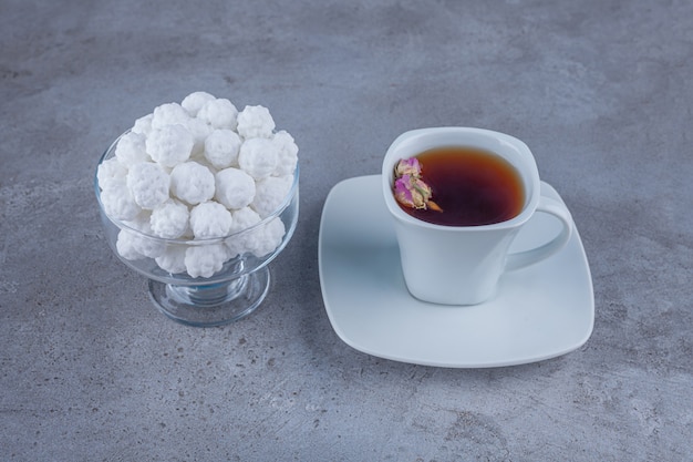 Kostenloses Foto schüssel weiße süße bonbons mit tasse tee auf steinoberfläche.