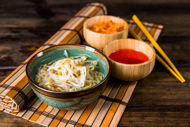 Schüsseln mit gekeimten Bohnen und roter Chili-Sauce mit Essstäbchen auf Tischset über dem Tisch