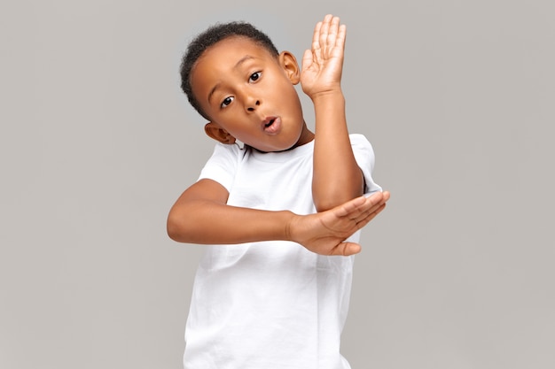 Schul-, Kinder-, Lern- und Bildungskonzept. Hübscher, selbstbewusster, dunkelhäutiger, ausgezeichneter Schüler, der die Hand hebt, als würde er im Unterricht am Schreibtisch sitzen, Wissen demonstrieren und Fragen beantworten