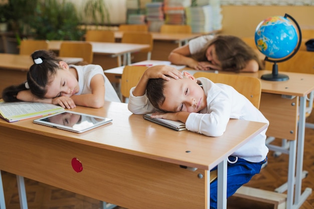 Schulkinder, die auf Schreibtischen liegen, klatschen