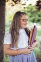 Kostenloses Foto schulmädchen in der uniform, die im garten mit büchern steht