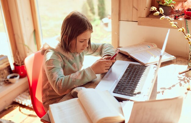 Schulmädchen macht Hausaufgaben zu Hause und tippt eine Nachricht auf ihrem Handy