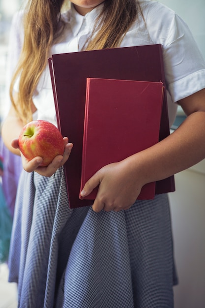 Schulmädchen mit Apfel und Büchern in den Händen