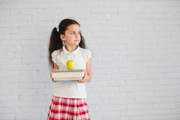 Schulmädchen stehend hält Bücher Apfel