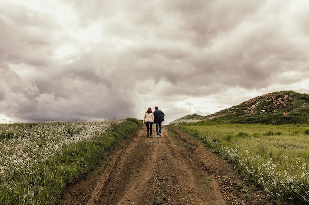 Schuss eines Mannes und einer Frau, die entlang eines Weges in einem Tal mit Blumen unter einem nebligen Himmel gehen