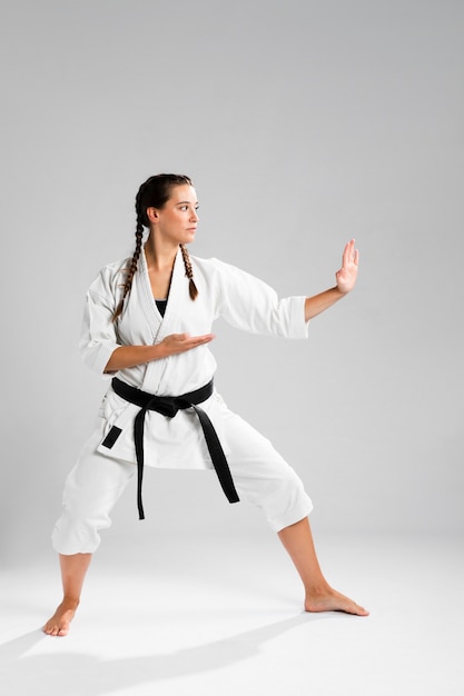 Schuss in voller Länge einer Frau mit übendem Karate des schwarzen Gürtels und des Kimonos