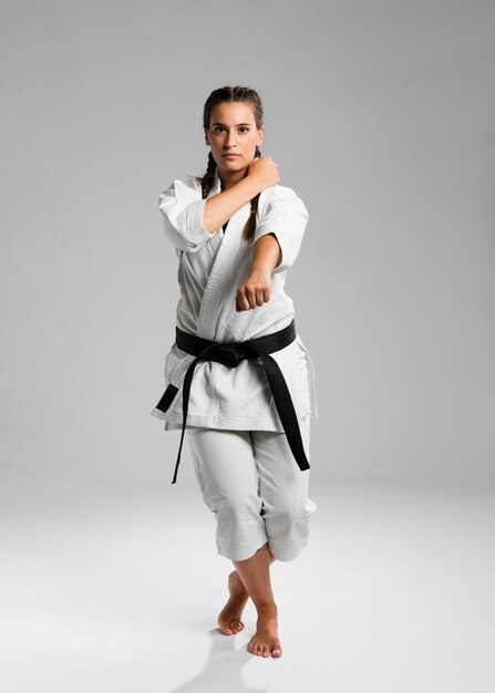 Schuss in voller Länge einer Frau mit übendem Karate des schwarzen Gürtels und des Kimonos