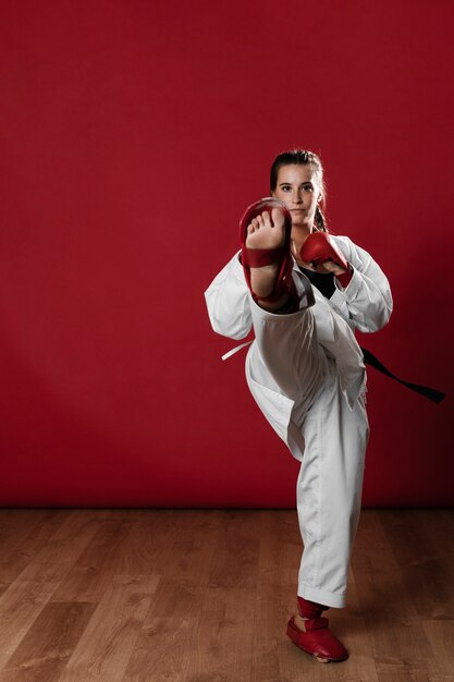 Schuss in voller Länge einer Frau mit übendem Karate des schwarzen Gürtels und des Kimonos