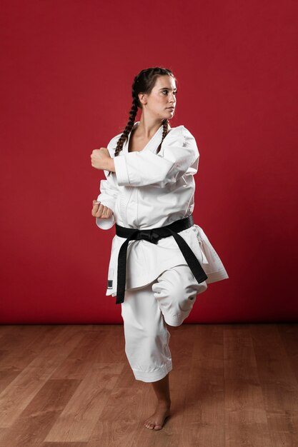 Schuss in voller Länge einer Frau mit übendem Karate des schwarzen Gürtels und des Kimonos