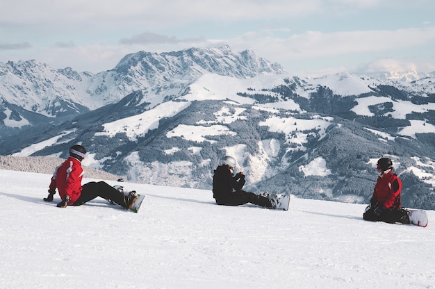 Kostenloses Foto schuss von snowboardern, die auf schnee sitzen und die weißen berge in tirol, österreich betrachten