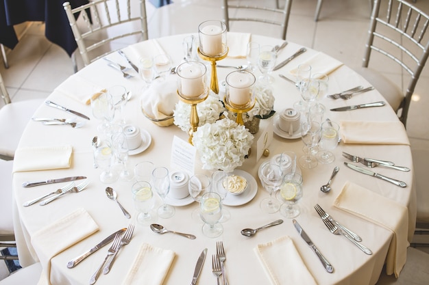 Schuss von weißen Blumensträußen und Stumpenkerzen in Goldkandelabern auf einem Hochzeitstisch