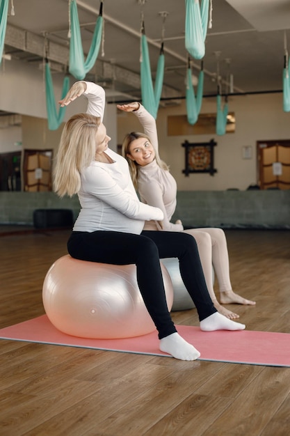 Schwangere Frau beim Yoga mit Personal Trainer Yoga-Trainer unterstützt schwangere Frau dabei Übungen mit einem Fitball Blonde schwangere Frau in weißen Kleidern