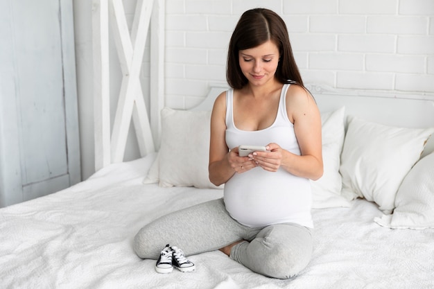 Schwangere Frau der Vorderansicht, die ihr Telefon überprüft