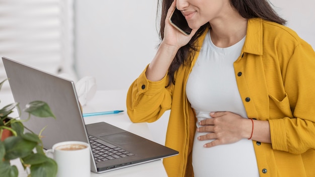 Schwangere Frau, die am Telefon mit Laptop spricht