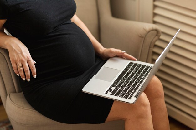 Schwangere Frau, die auf einem Stuhl sitzt und an Laptop arbeitet